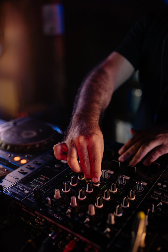 Close-up of a DJs hands adjusting an audio mixer in a dimly lit club scene.